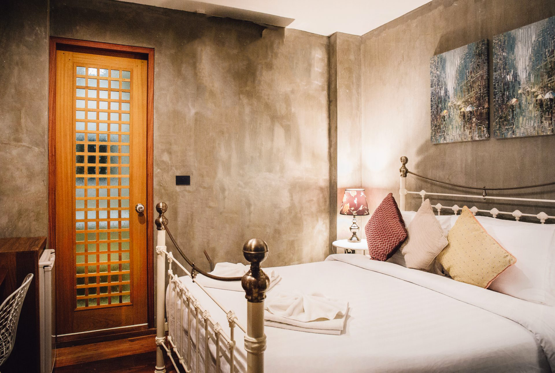 Chambre double éco-confort de Lompoul Nature, avec murs en béton ciré, lit en fer forgé blanc, éclairage chaleureux et décoration minimaliste.