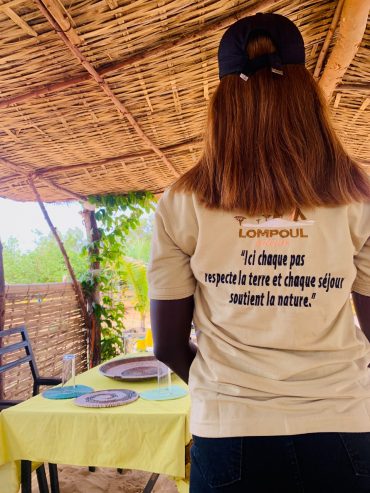 Membre de l’équipe de Lompoul Nature préparant une table pour un repas de cuisine sénégalaise dans un cadre naturel à Lompoul
