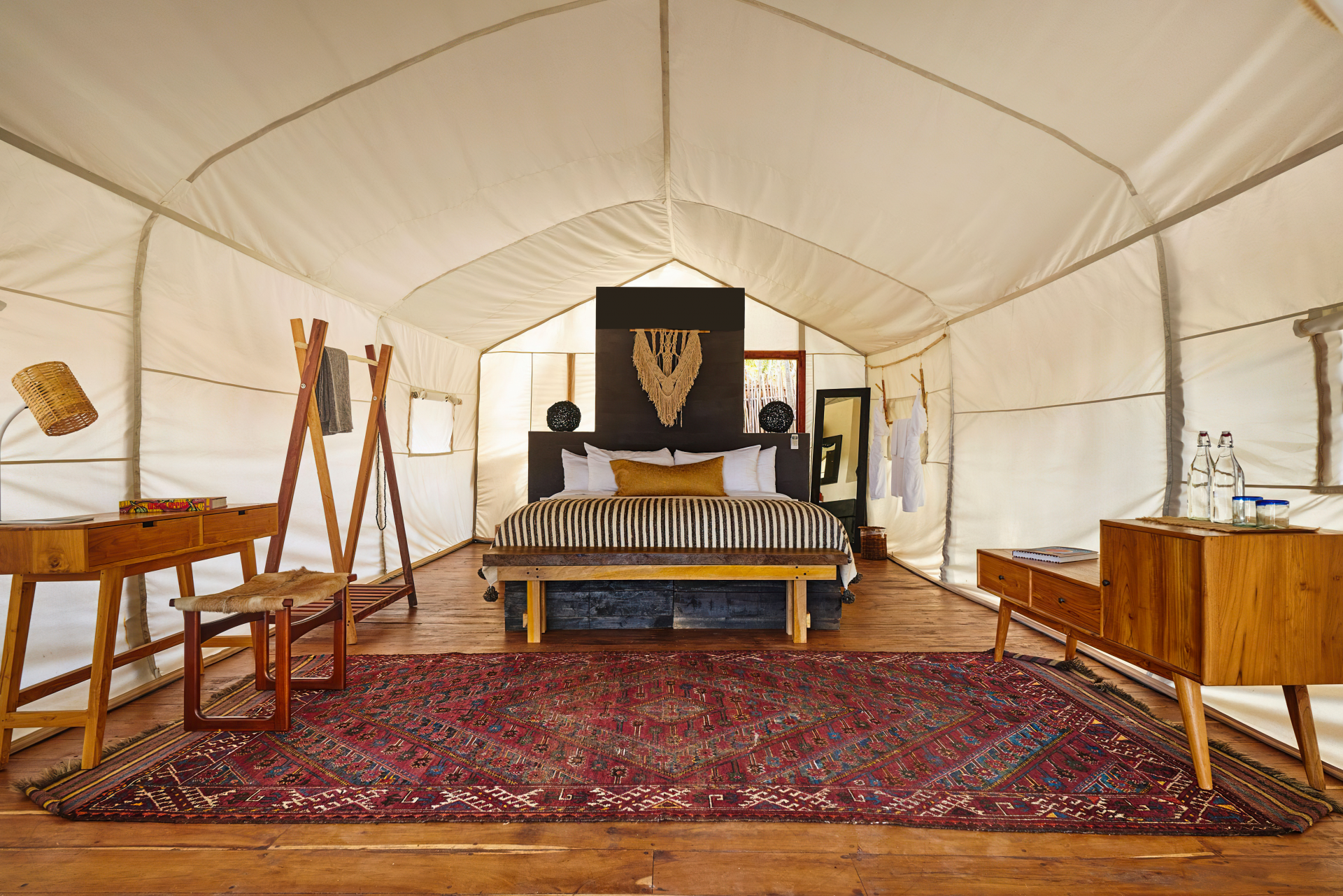 Intérieur d’une tente luxueuse de Lompoul Nature, décorée avec des meubles en bois, un grand lit central, un tapis berbère rouge et une ambiance chaleureuse rappelant le glamping dans le désert du Lompoul.