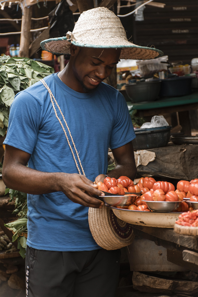 Un homme souriant tient un grand plateau garni de petits plats de tomates fraîches, dans le cadre naturel du campement Lompoul Nature.
